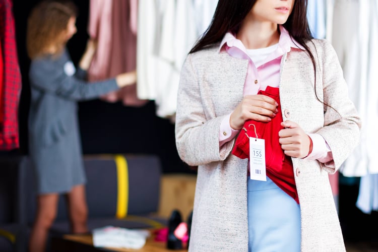 Woman hiding a red clothing item with the tag still on in her jacket. 