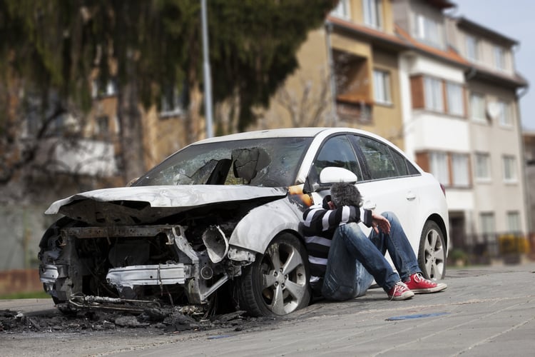 Man sits on the ground next to his totaled car